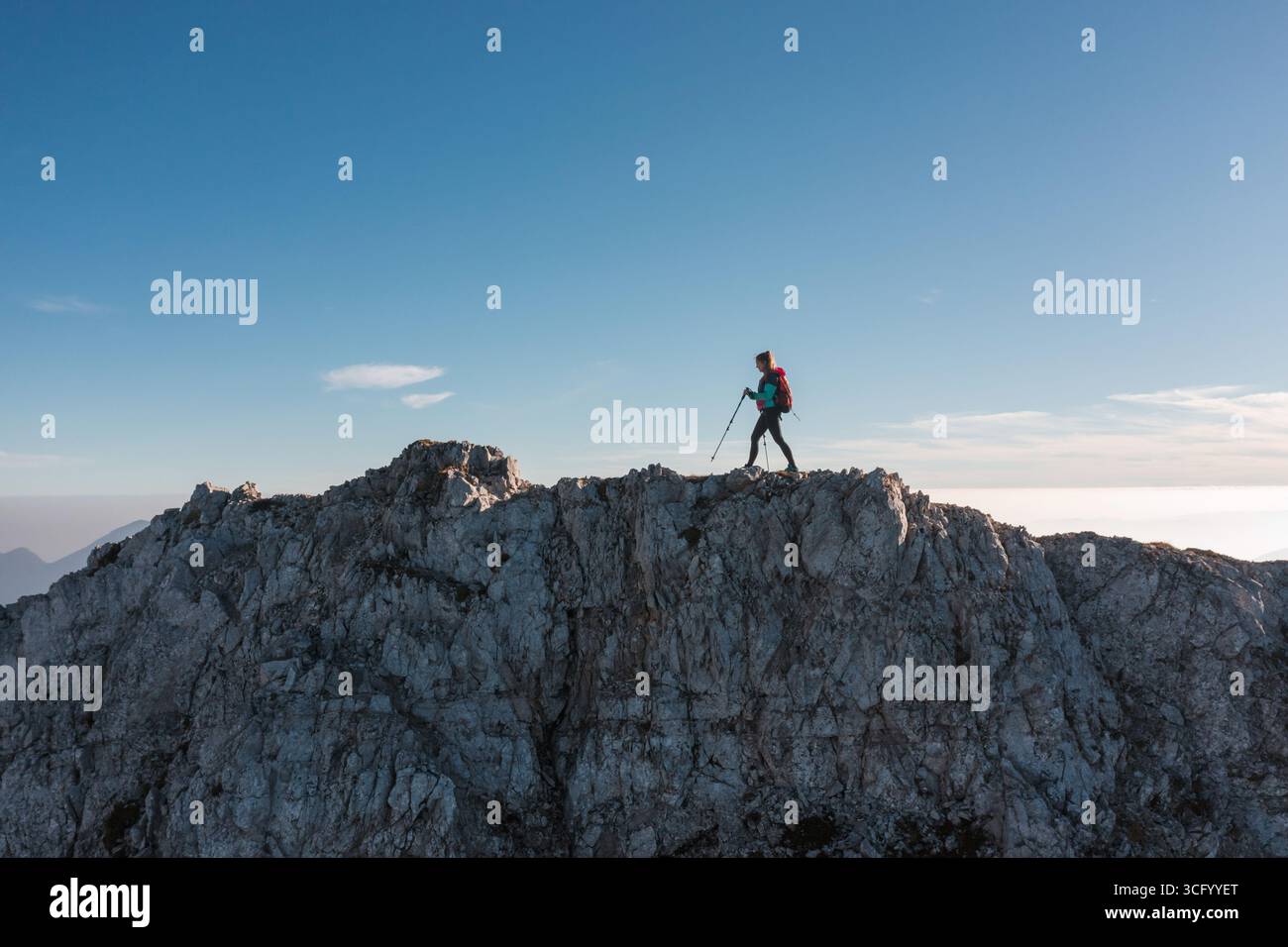 Wanderer stehen auf einem felsigen Gipfel bei Sonnenaufgang und bewundern atemberaubende Aussichten am klaren Morgenhimmel. Stockfoto