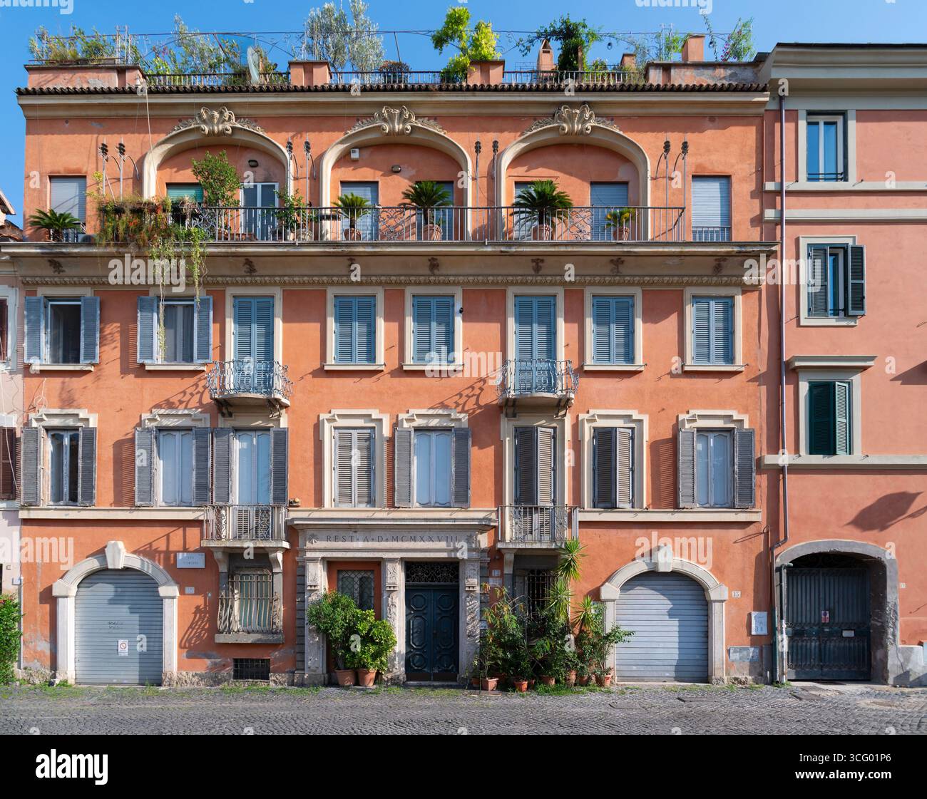 Römische Architektur, oranges Gebäude mit grünen Fensterläden und zahlreichen Balkonen in einer Kopfsteinpflasterstraße im historischen Zentrum von Rom, Italien Stockfoto