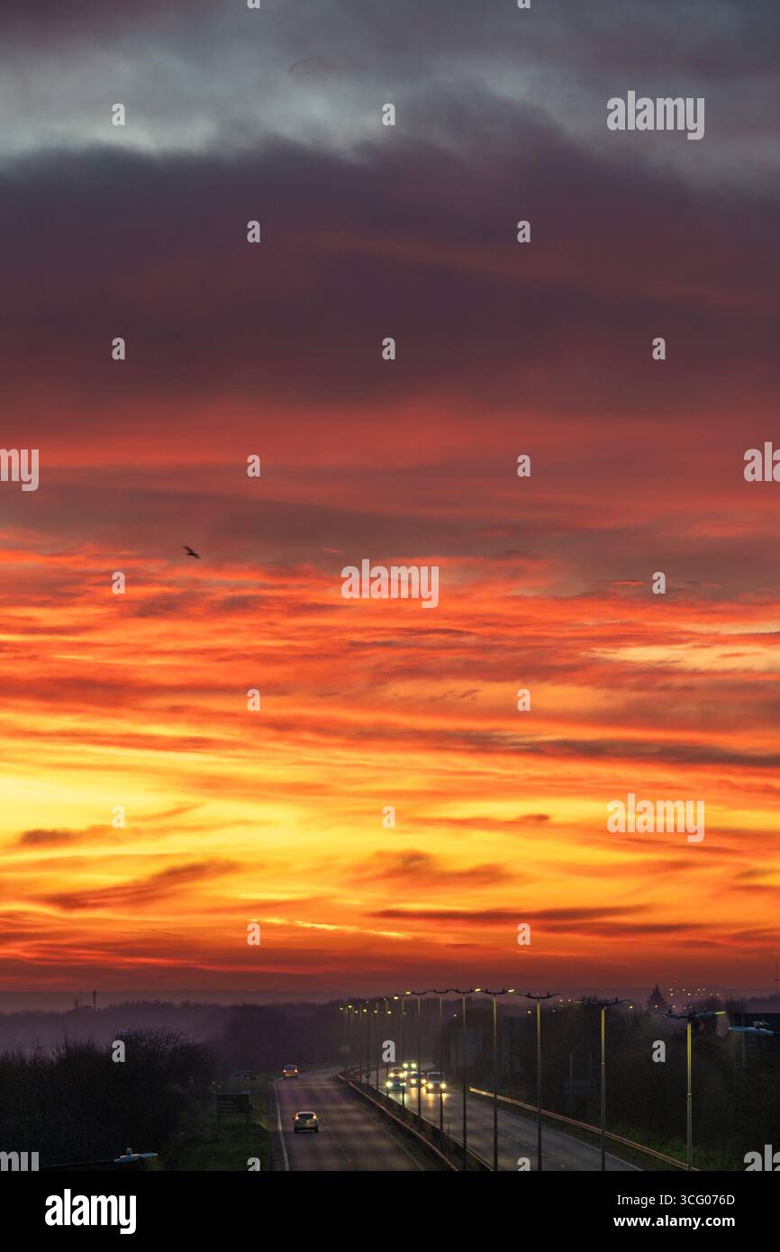Dramatischer Morgenhimmel, gelb und orange, mit Wolken, die von unten durch die noch aufgehende Sonne über dem Thanet Way, A299, in Herne Bay beleuchtet werden Stockfoto