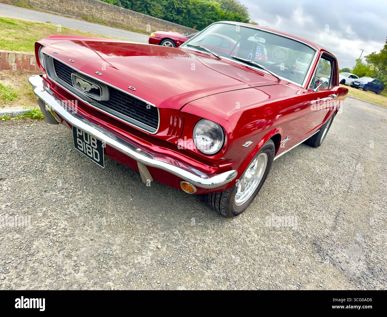 Klassischer roter Ford Mustang aus dem Jahr 1966, der auf einer Landstraße mit bewölktem Himmel im Hintergrund geparkt ist - Smartphone-aufgenommenes Stockfoto Klassischer roter Ford Mustang aus dem Jahr 1966, der auf einer Landstraße mit bewölktem Himmel im Hintergrund geparkt ist - Smartphone-aufgenommenes Stockfoto