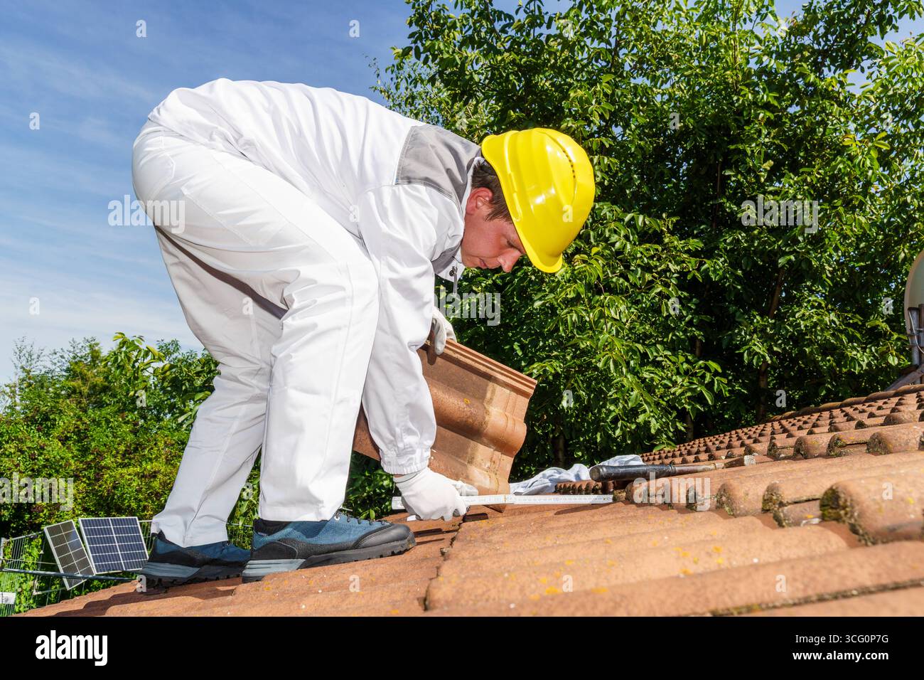 Bayern, Deutschland - 25. August 2025: Ein Dachdecker arbeitet intensiv auf dem Dach und misst die Position der Fliesen. Das Bild zeigt die Präzision und die körperliche Arbeit, die beim Bedachen und Ersetzen von Fliesen - einem klassischen Fachhandel - erforderlich ist. *** Ein Dachdecker arbeitet konzentriert auf dem Dach und messen die Position der Ziegel. Das Bild zeigt die Präzision und körperliche Arbeit beim Dachdecken und einem Ziegeltausch - ein klassischer Handwerksberuf. Stockfoto
