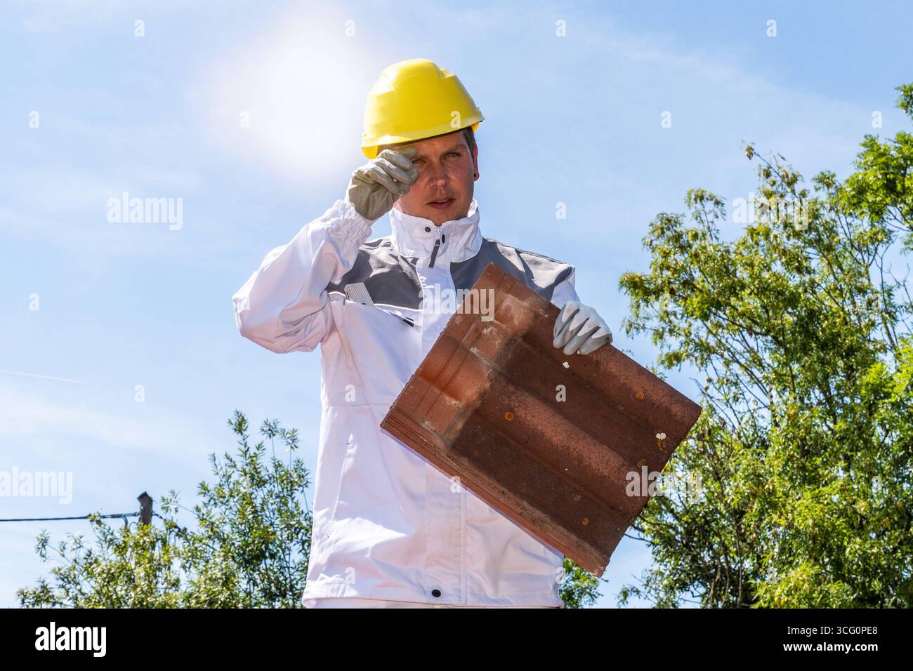 Bayern, Deutschland - 25. August 2025: Ein Bauarbeiter steht während einer Hitzewelle auf einem Dach in der glühenden Sonne. Das Bild zeigt die körperliche Belastung, Risiken und Herausforderungen, die bei der Arbeit auf einer Baustelle im Sommer entstehen. *** Ein Bauarbeiter auf dem Dach stehen in der prallen Sonne während einer Hitzewelle. Das Bild verdeutlicht die körperliche Belastung, Risiken und Herausforderungen von Arbeiten im Sommer auf dem Bau. Stockfoto