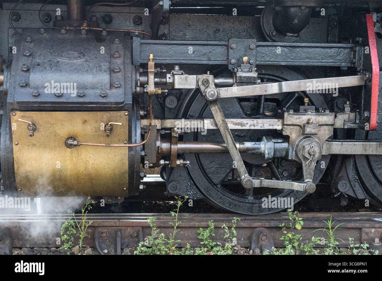 Nahaufnahme der Antriebsräder und Pleuelstangen einer alten Dampflokomotive mit gelbem Zylindergehäuse und schwarzen mechanischen Komponenten Stockfoto