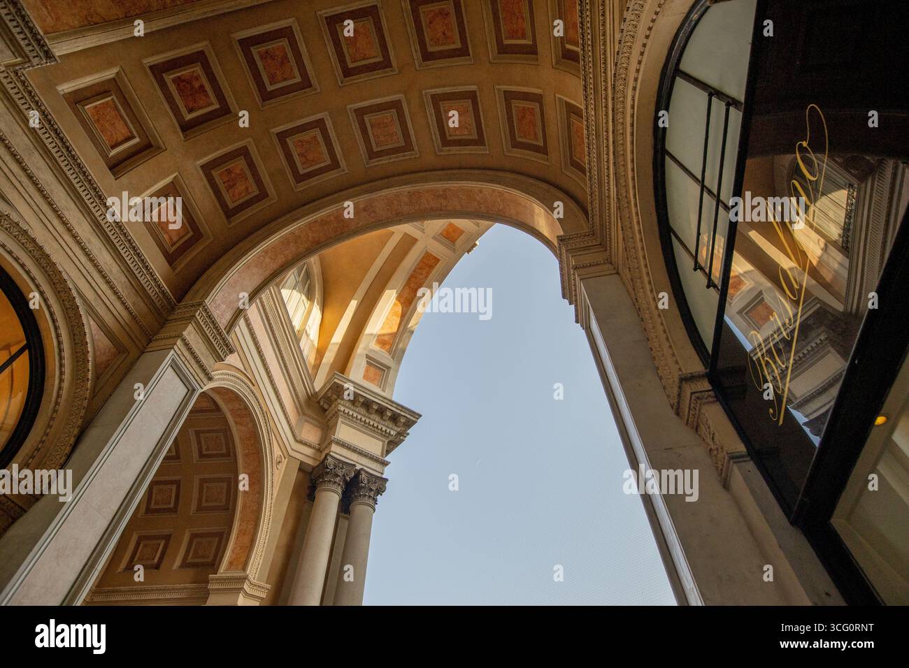 Beeindruckender Blick auf die Bögen der Galleria Vittorio Emanuele II, die sich in Richtung eines lebendigen Himmels erstrecken, während Besucher den eleganten Raum erkunden. Stockfoto