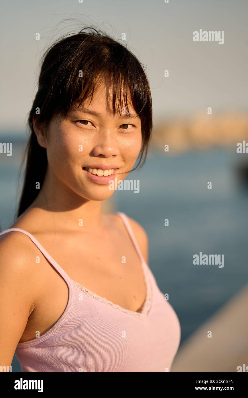 Junge asiatische Frau lächelt am Meer bei Sonnenuntergang Stockfoto