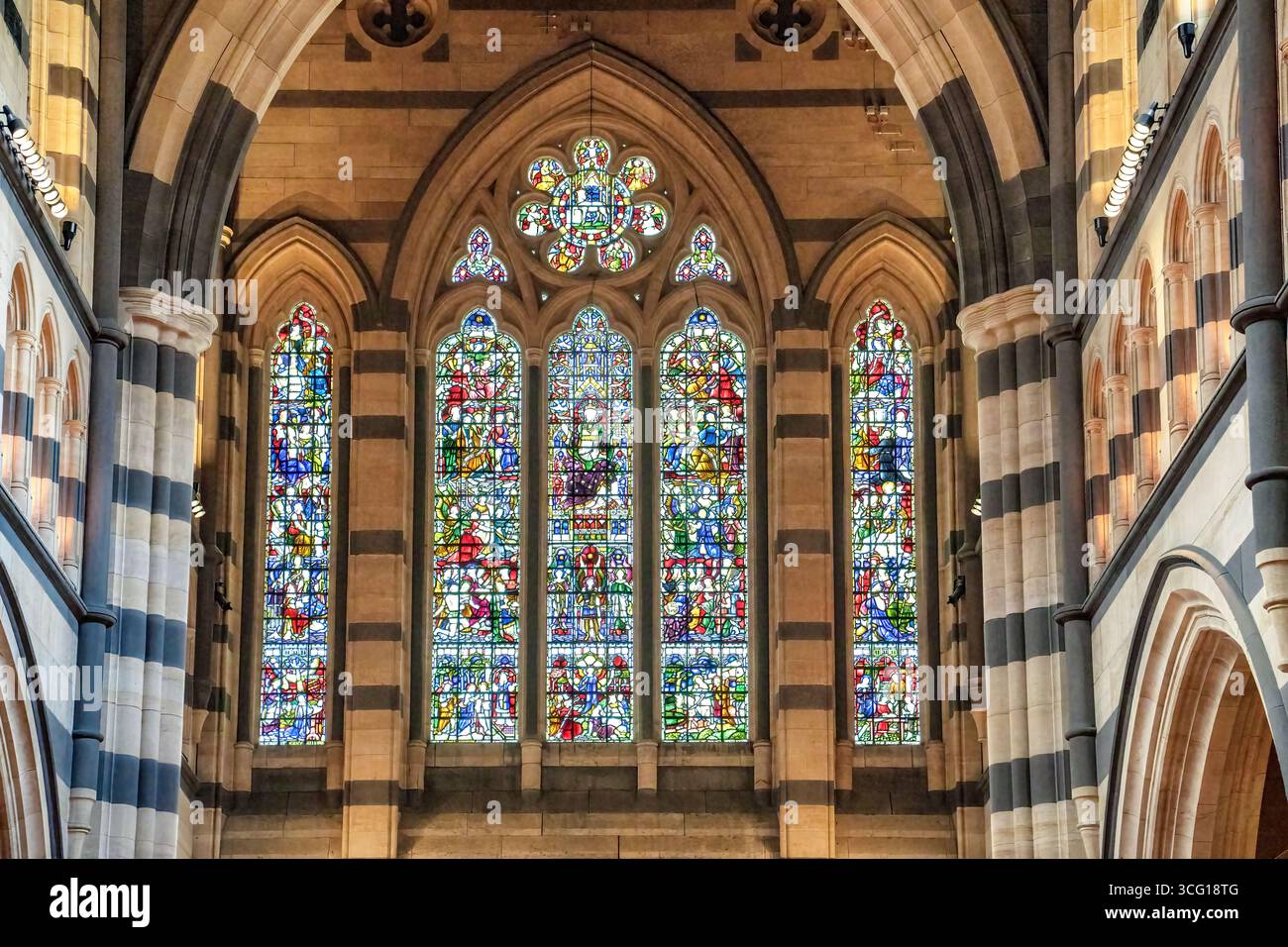 Buntglasfenster in der anglikanischen St. Paul's Cathedral, umgeben von Steinbögen und komplexen architektonischen Details in Melbourne, Australien. Stockfoto