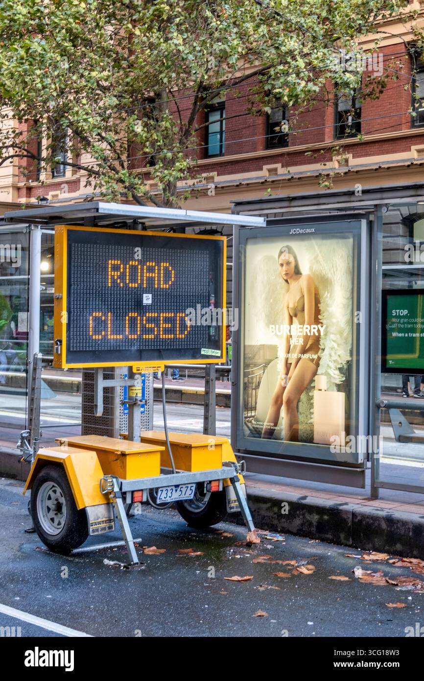 Elektronisches Schild „Road Closed“ neben einer Modewerbung entlang der Flinders Street in Melbourne, Australien. Stockfoto