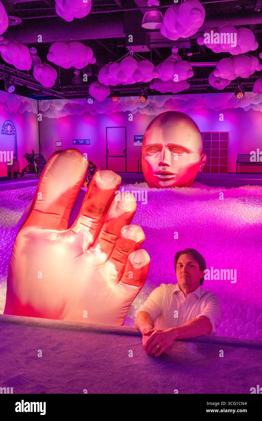 Eine faszinierende Kunstinstallation mit einer riesigen Hand und einem Gesicht, beleuchtet in leuchtendem Rosa und Lila, schafft eine immersive Atmosphäre für Besucher. Stockfoto