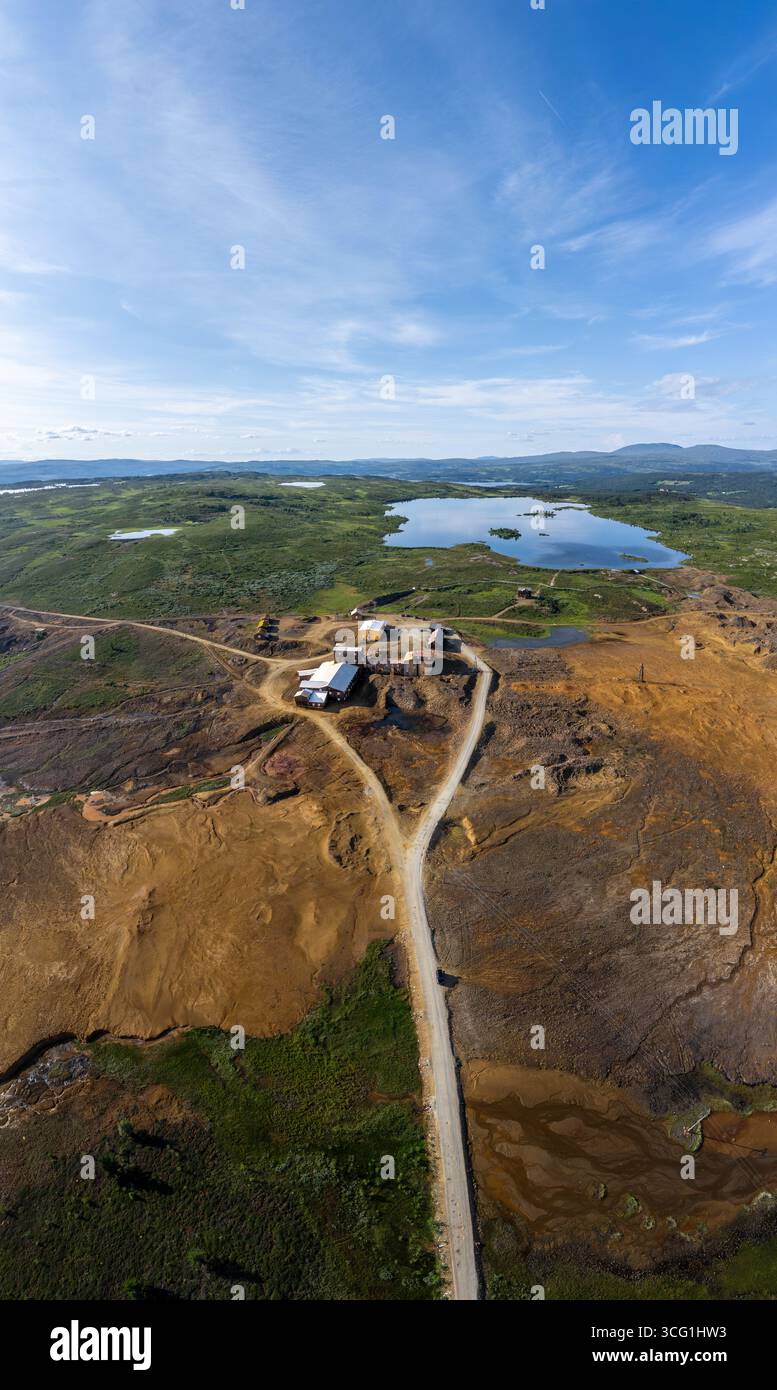 Weite, erdige Landschaft einer verlassenen Kupfermine in Røros, Orangentöne und ein ruhiger blauer See umgeben von frischem Grün. Vertikale Antennenansicht Stockfoto