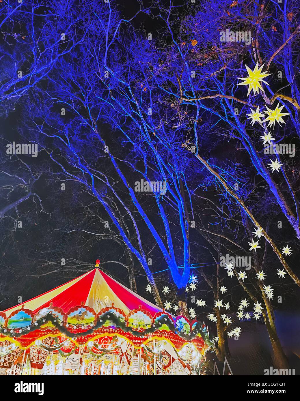 Weihnachtsmarkt Karussell bei Nacht mit gelben Sternlaternen und blau beleuchteten Winterbäumen, Köln, Nordrhein-Westfalen, Deutschland. - Smartphone-aufgenommenes Stockfoto