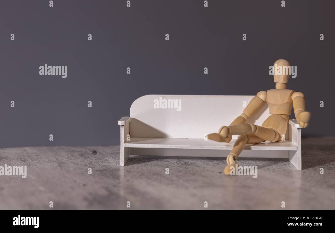 Holzmann und Buch. Holzfigur Sitzend. Fröhliche Holzpuppe auf blauem Hintergrund mit einem Buch. Bücher Lesen Zeigt Lernen. Bildungskonzept. Stockfoto
