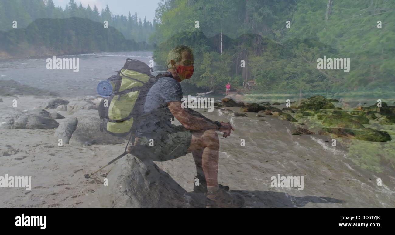 Sitzender Wanderer mit roter Maske auf gefallenem Baumstamm am Fluss, mit Rucksack mit gerolltem Polster Stockfoto