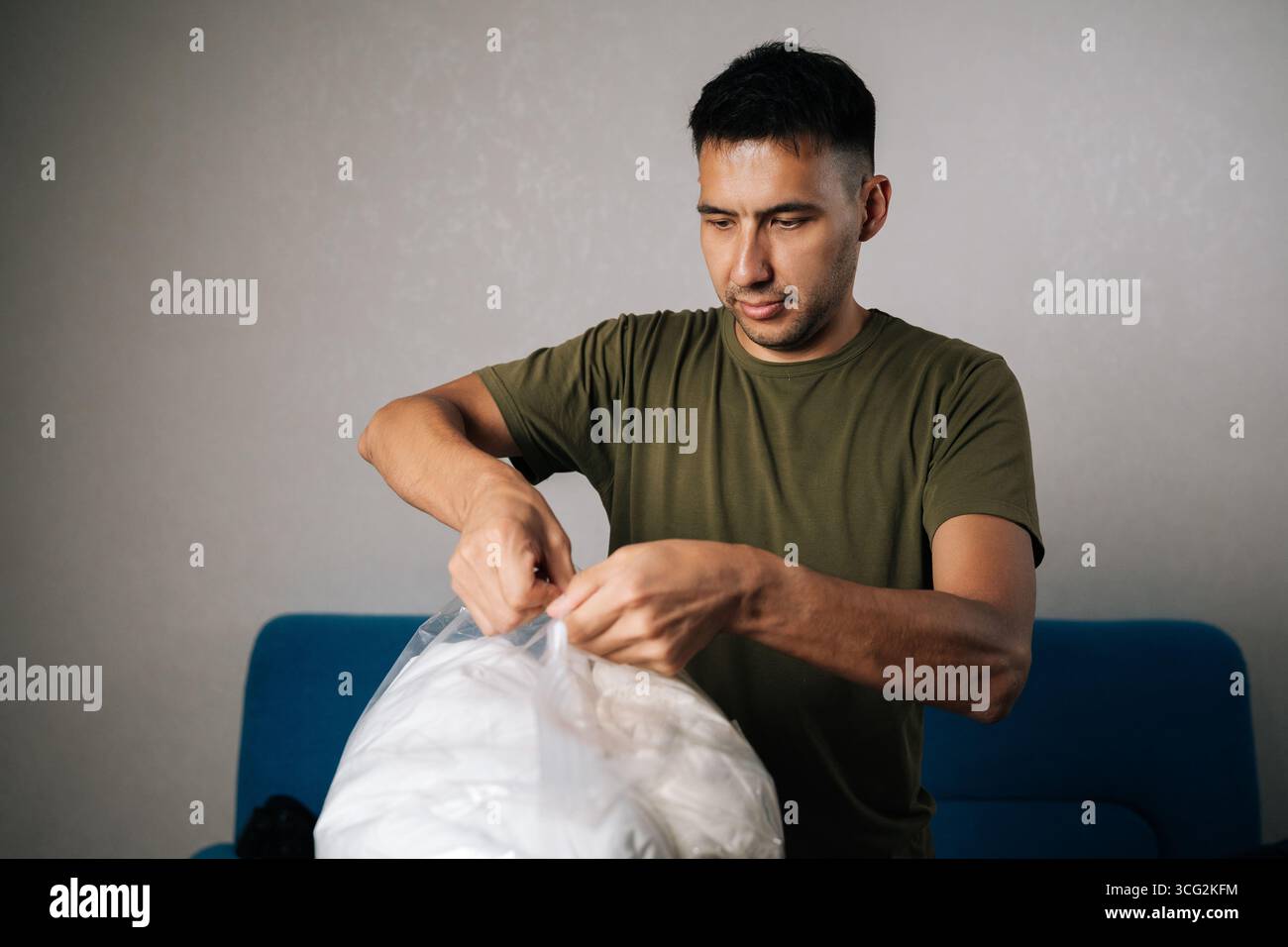 Fokussierter junger Mann, der große transparente Vakuumbeutel mit weißer Bettwäsche schließt, mit doppeltem Reißverschluss, um eine luftdichte Abdichtung für optimale Ergebnisse zu schaffen Stockfoto