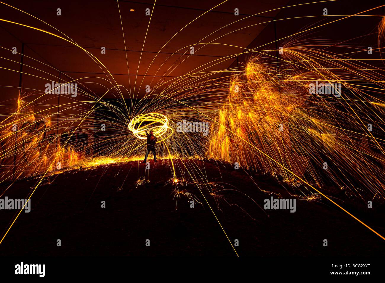 Ein Darsteller schwingt eine feurige Fackel und schafft während der Nacht leuchtende Lichtspuren in einer dunklen, urbanen Umgebung. Stockfoto