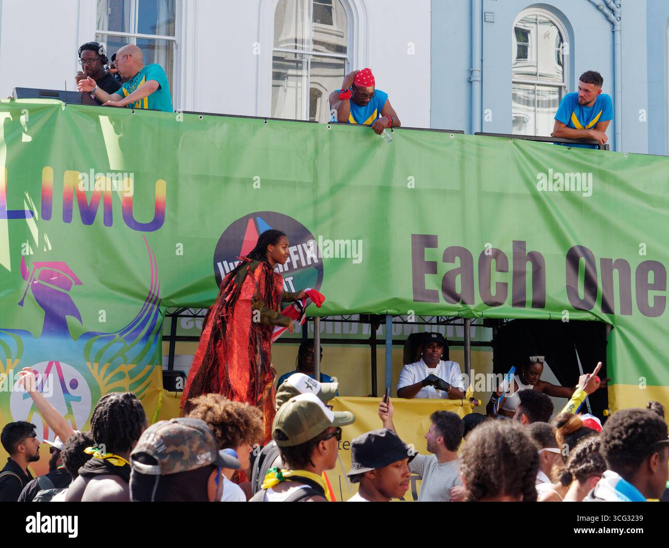 Frau auf Stelzen in rotem Mantel neben einem Wagen inmitten der Menschenmassen während des Notting Hill Carnival in London. England, 25. August 2025 Stockfoto