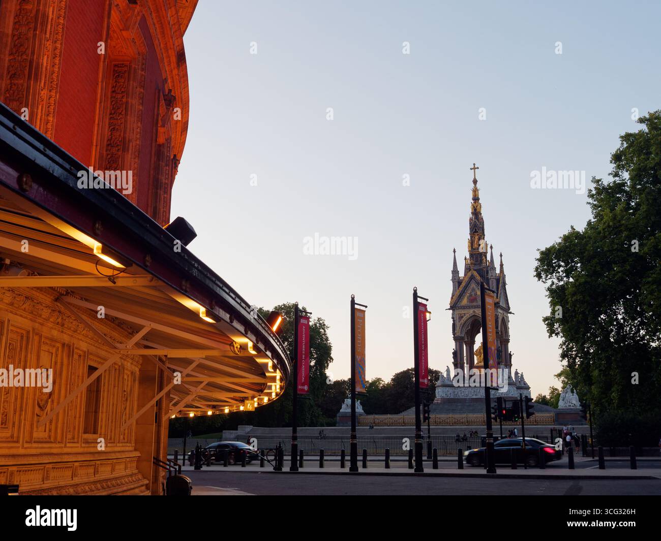 Albert Memorial rechts an einem Sommerabend in London, wenn Autos vorbeifahren und ein Teil der Royal Albert Hall links ist . August 2025 Stockfoto