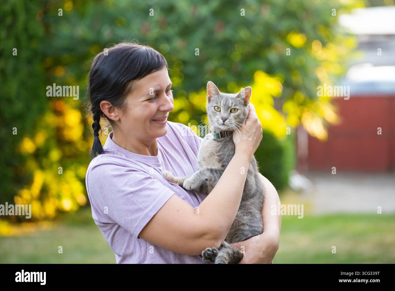 Frau mittleren Alters hält ihre süße Katze draußen. Stockfoto