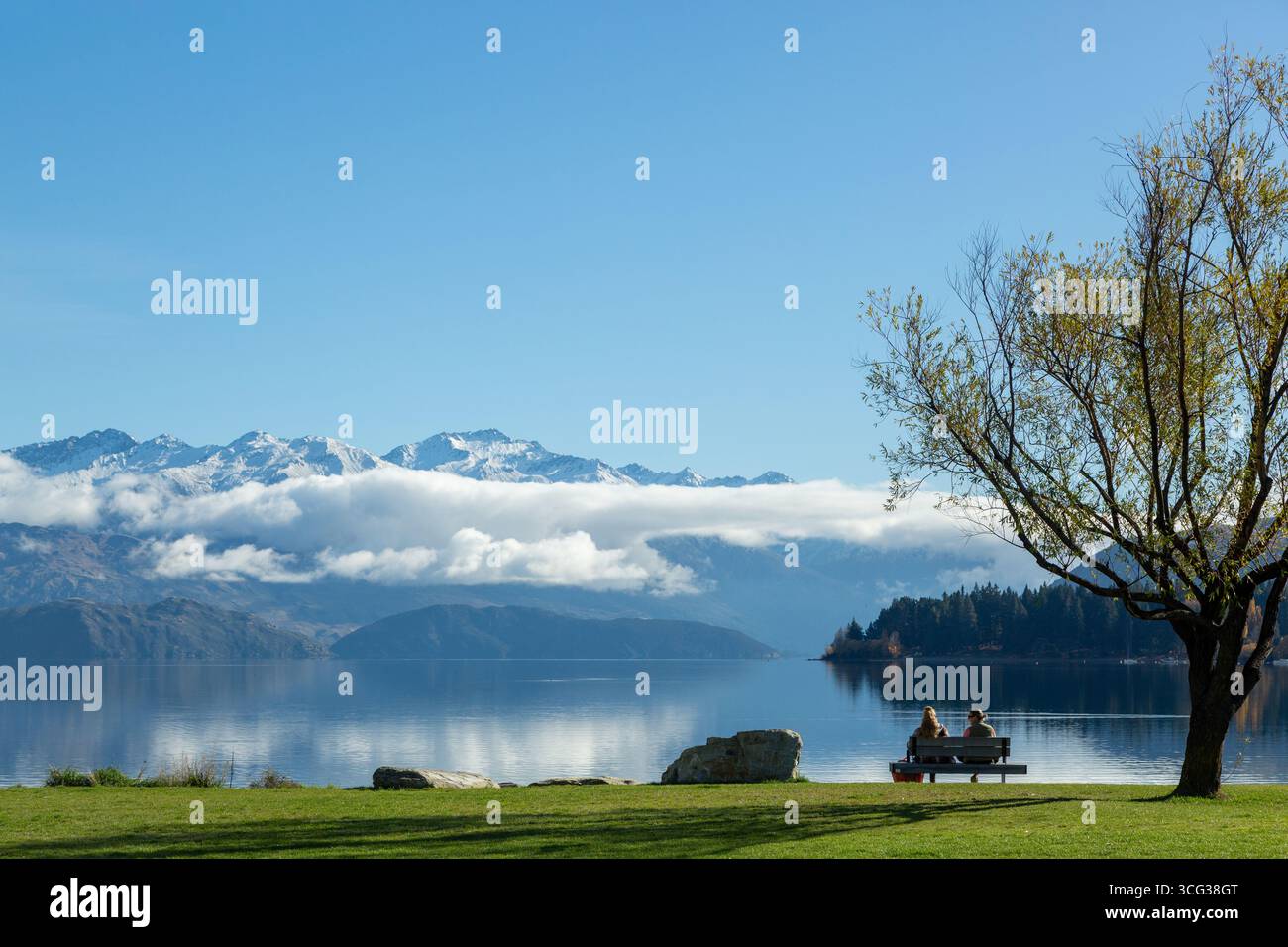 Zwei Personen sitzen auf einer Parkbank mit Blick auf die südlichen Alpen und den Lake Wanaka an einem sonnigen Herbsttag in Otago, Neuseeland Stockfoto