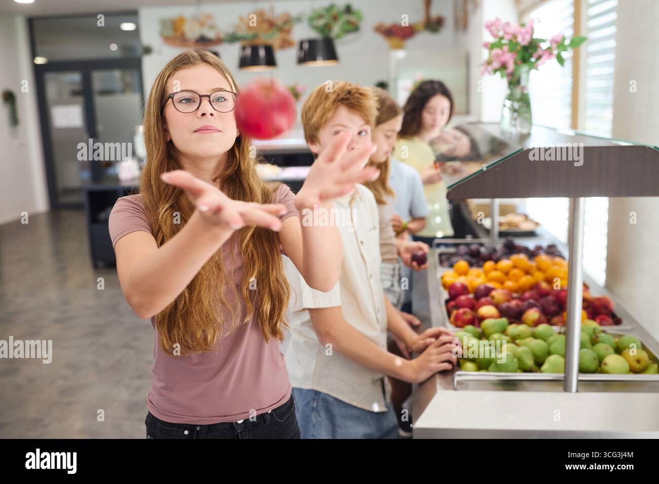 Eine Gruppe von Schülern versammelt sich um eine Cafeteria Obststation, wählt aus einer Reihe von frischen Produkten, hebt Initiativen für gesunde Ernährung in Schulen hervor, Stockfoto