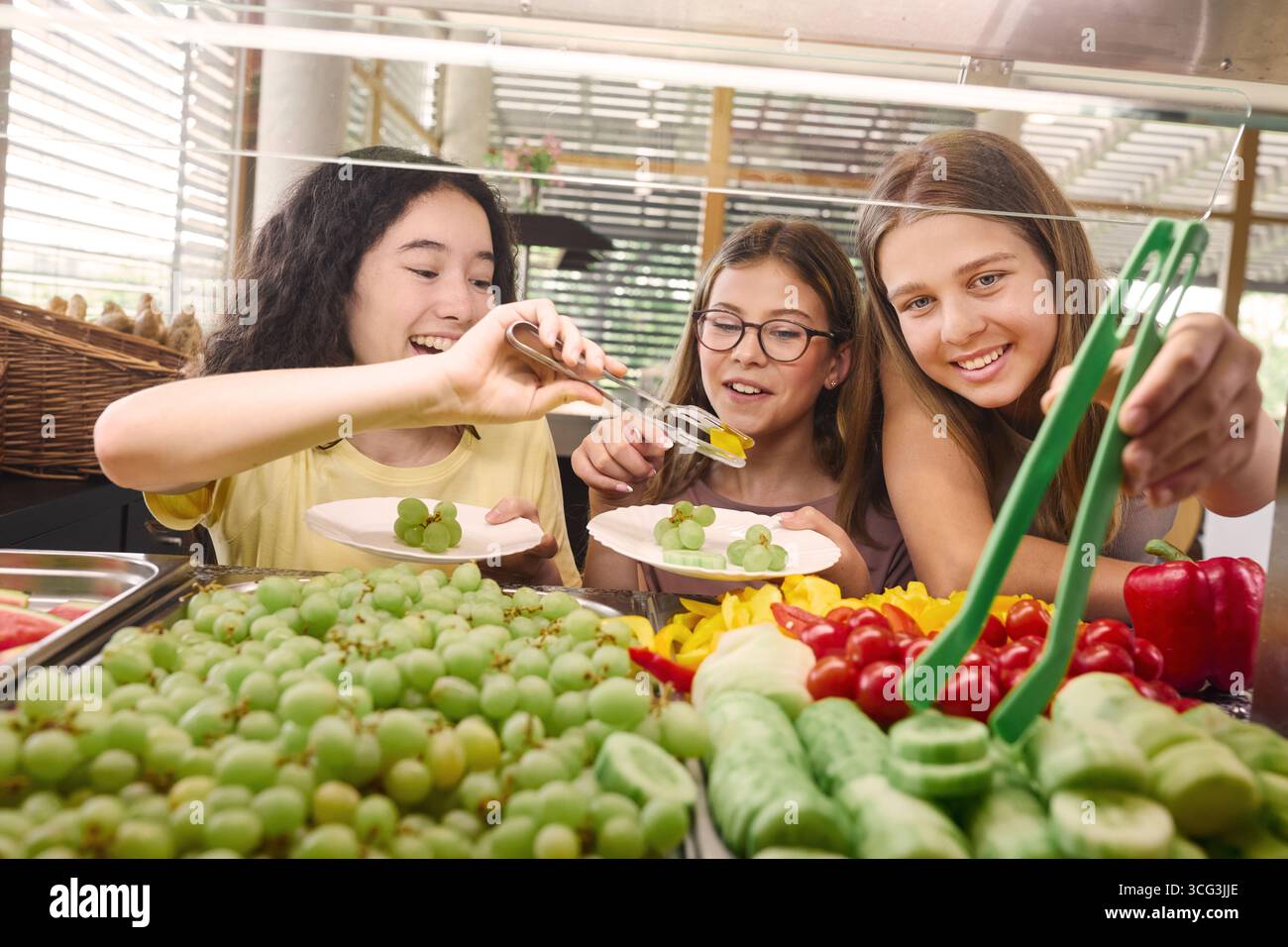 Drei Kinder genießen gesunde Speisen wie Obst und Gemüse aus einer Schulcafeteria zu pflücken. Eine fröhliche, gesunde Ernährung Umwelt Promot Stockfoto