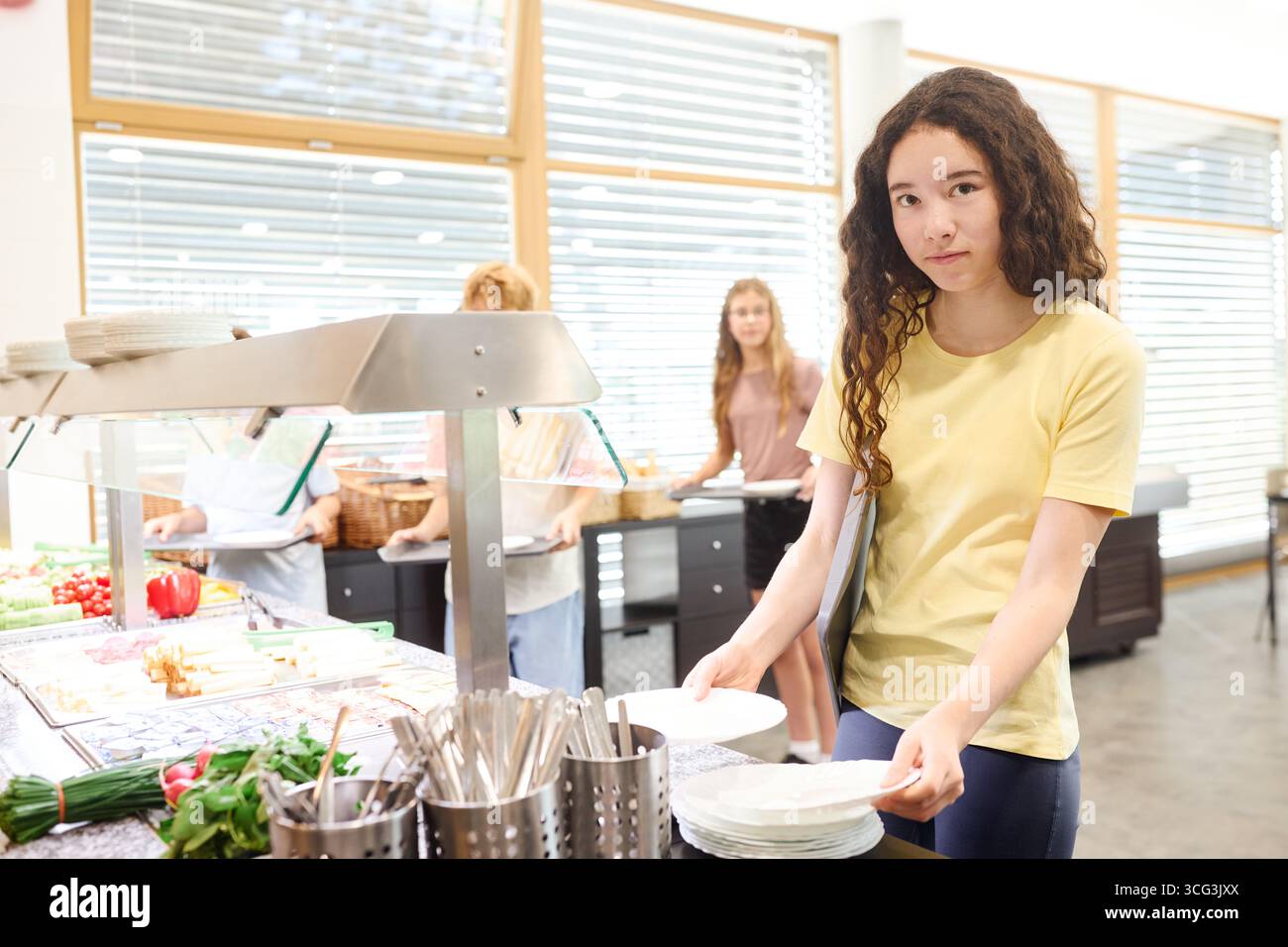 Eine Gruppe von Schülern wählt Gerichte aus einer Serviertheke in einer sauberen, gut beleuchteten Cafeteria, in der frische Produkte und eine einladende Umgebung präsentiert werden. Stockfoto