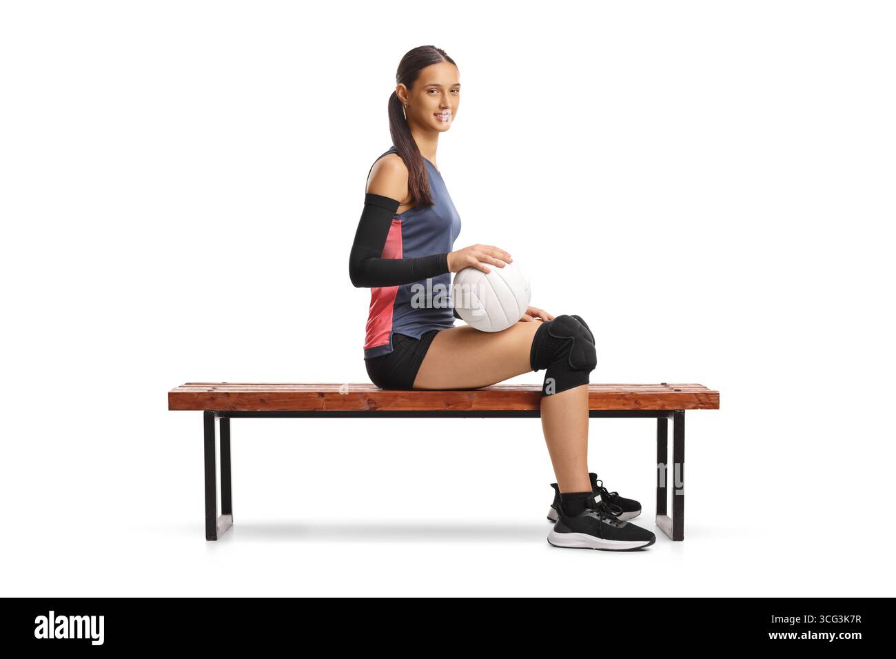 Junge weibliche Atlete, die einen Volleyball hält und auf einer Bank sitzt, isoliert auf weißem Hintergrund Stockfoto