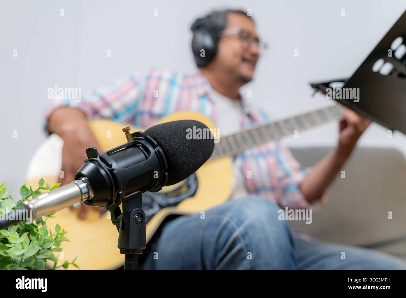 Ein junger Mann sitzt zu Hause, spielt Gitarre und schreibt Musik, zeigt Kreativität, Inspiration und die Freude, Songs in einem gemütlichen Raum zu komponieren Stockfoto