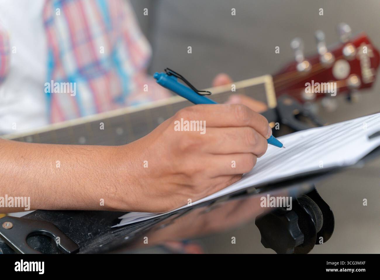 Ein junger Mann sitzt zu Hause, spielt Gitarre und schreibt Musik, zeigt Kreativität, Inspiration und die Freude, Songs in einem gemütlichen Raum zu komponieren Stockfoto