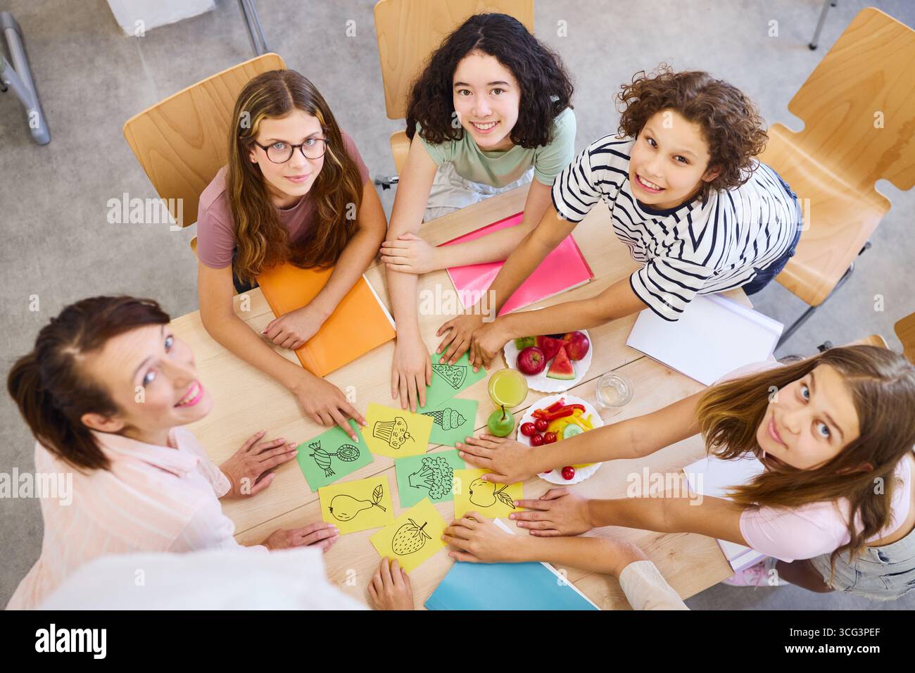 Eine Gruppe von Schülern und ein Lehrer nehmen an unterhaltsamen pädagogischen Aktivitäten teil, während sie gesunde Snacks in einer Schule essen, Teamarbeit fördern, lernen, Stockfoto