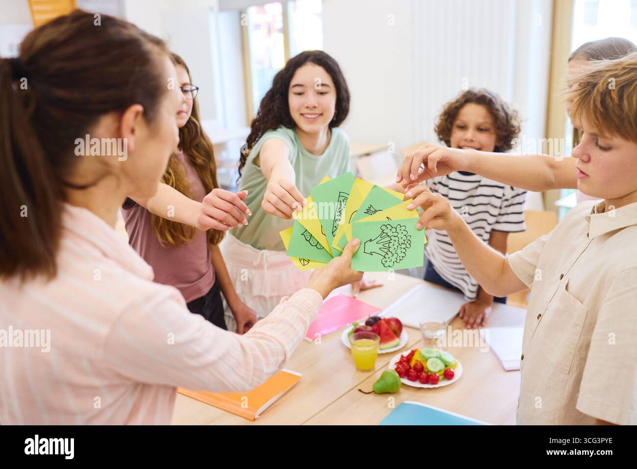 Eine Gruppe von Schülern, die bunte Zeichnungen während eines gesunden Essens in ihrer Schulcafeteria teilen. Die Atmosphäre ist freundlich und interaktiv, W Stockfoto