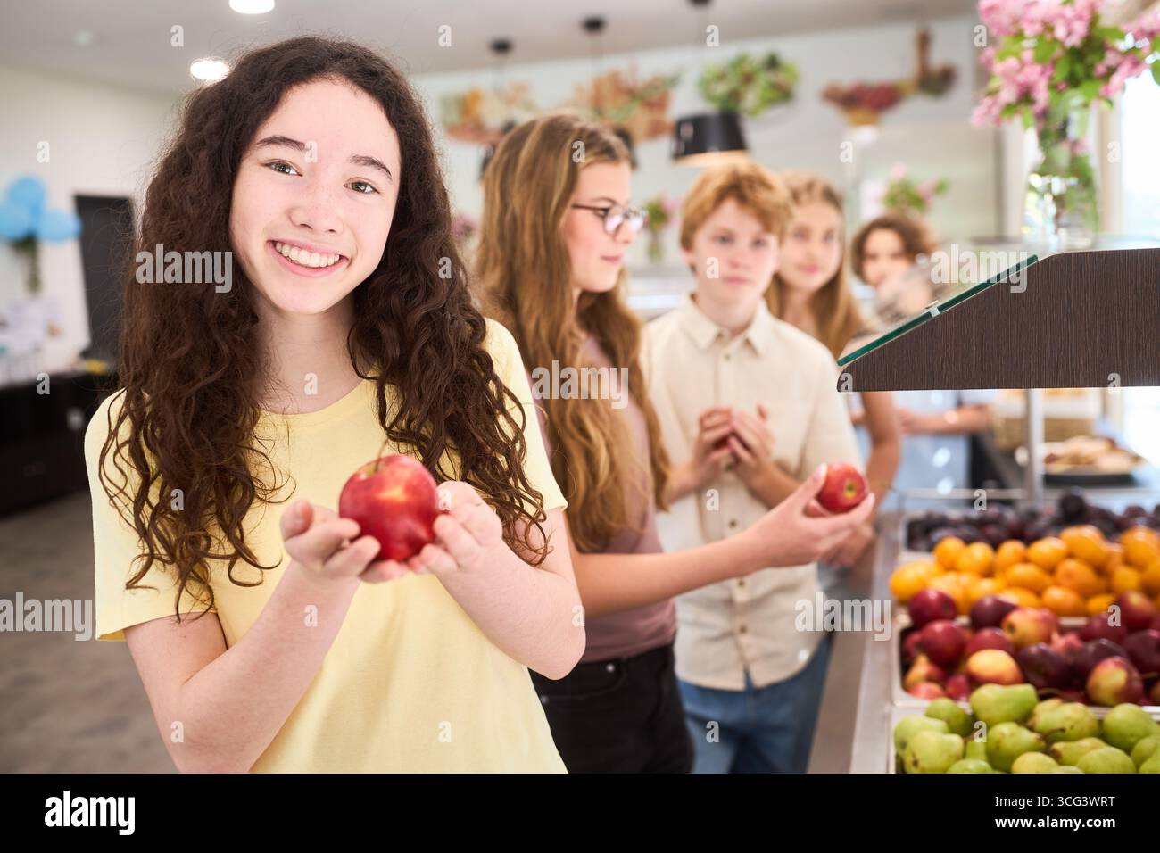 Eine Gruppe fröhlicher Schüler wählt frische Äpfel und Früchte in einer hellen Cafeteria. Fördert gesunde Essgewohnheiten und zeigt Schülerinteraktionen in Stockfoto