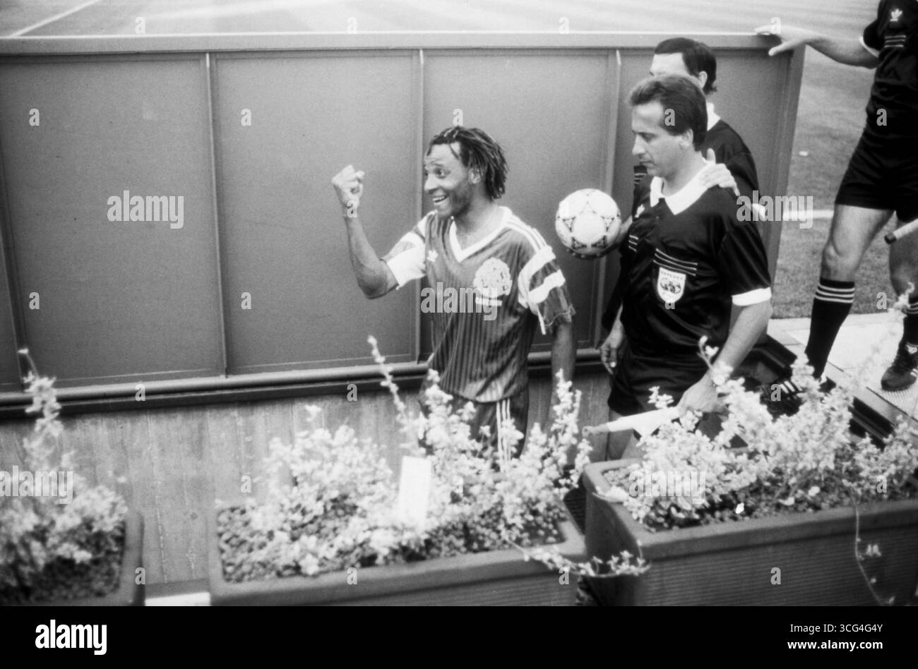 Cyrille Makanaky, Mittelfeldspieler der kamerunischen Nationalmannschaft, jubelt nach dem Sieg über Rumänien bei der Fußball-Weltmeisterschaft 1990. Der Spieler verlässt mit erhobener Faust und einem strahlenden Lächeln den Innenraum des Stadions, flankiert von Schiedsrichtern. Stockfoto