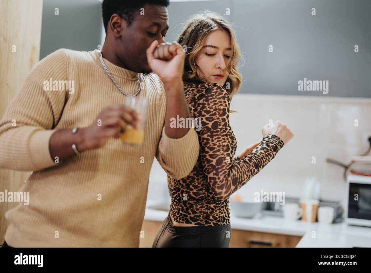 Ein vielseitiges Paar, das einen verspielten Moment genießt, während es in einer modernen Küche tanzt Stockfoto