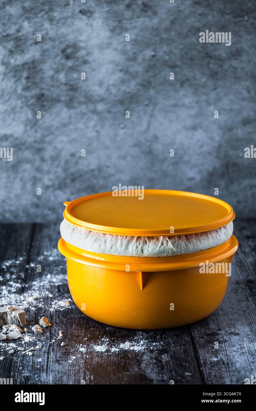 Schüssel mit aufsteigendem Hefeteig und frischer Hefe auf dem dunklen Tisch, Kopierraum, vertikal Stockfoto