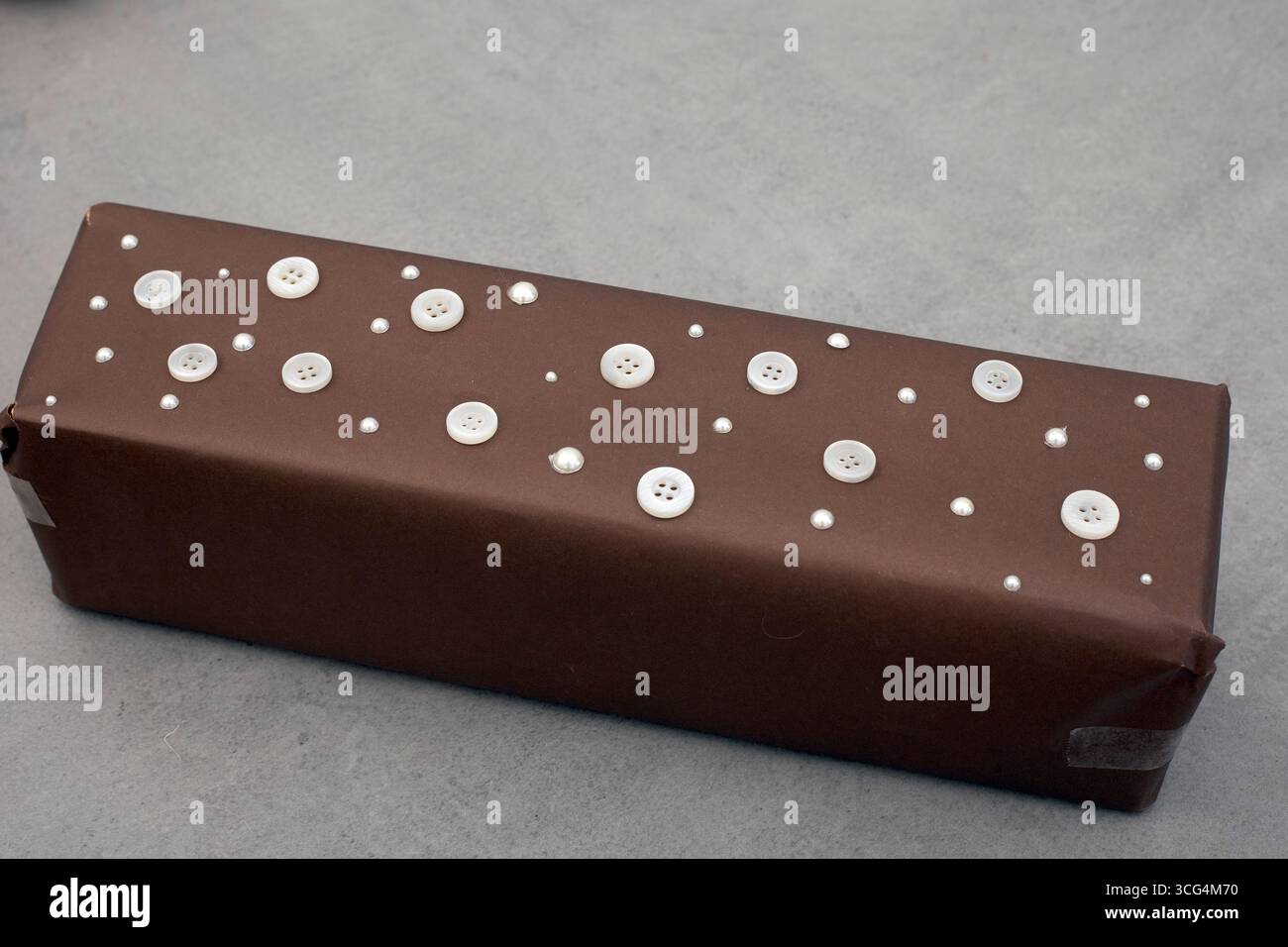 Geschenkverpackung für einen männlicheren Look. Braune Papierfolie mit weißen Knöpfen und kleinen Perlstickern. Ein einzigartiger und anderer Look Stockfoto