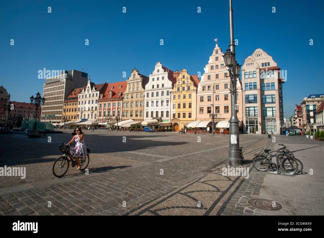 Eine Frau fährt mit dem Fahrrad durch den Marktplatz an einem sonnigen Tag in Breslau, Polen. Stockfoto