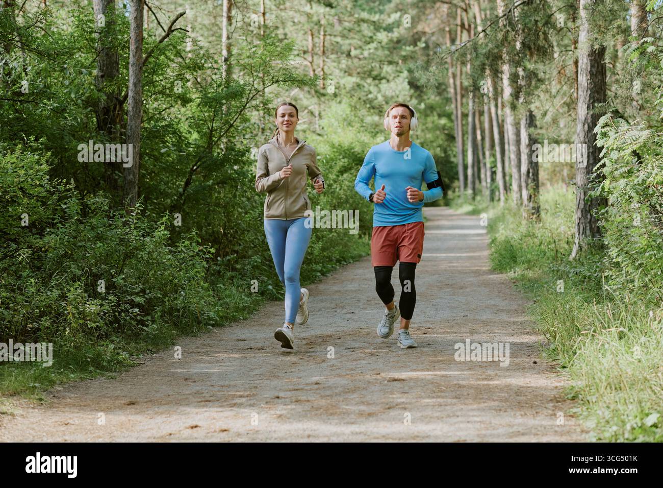 Kaukasische junge Erwachsene joggen gemeinsam auf dem Forest Trail in der Morgensonne Stockfoto