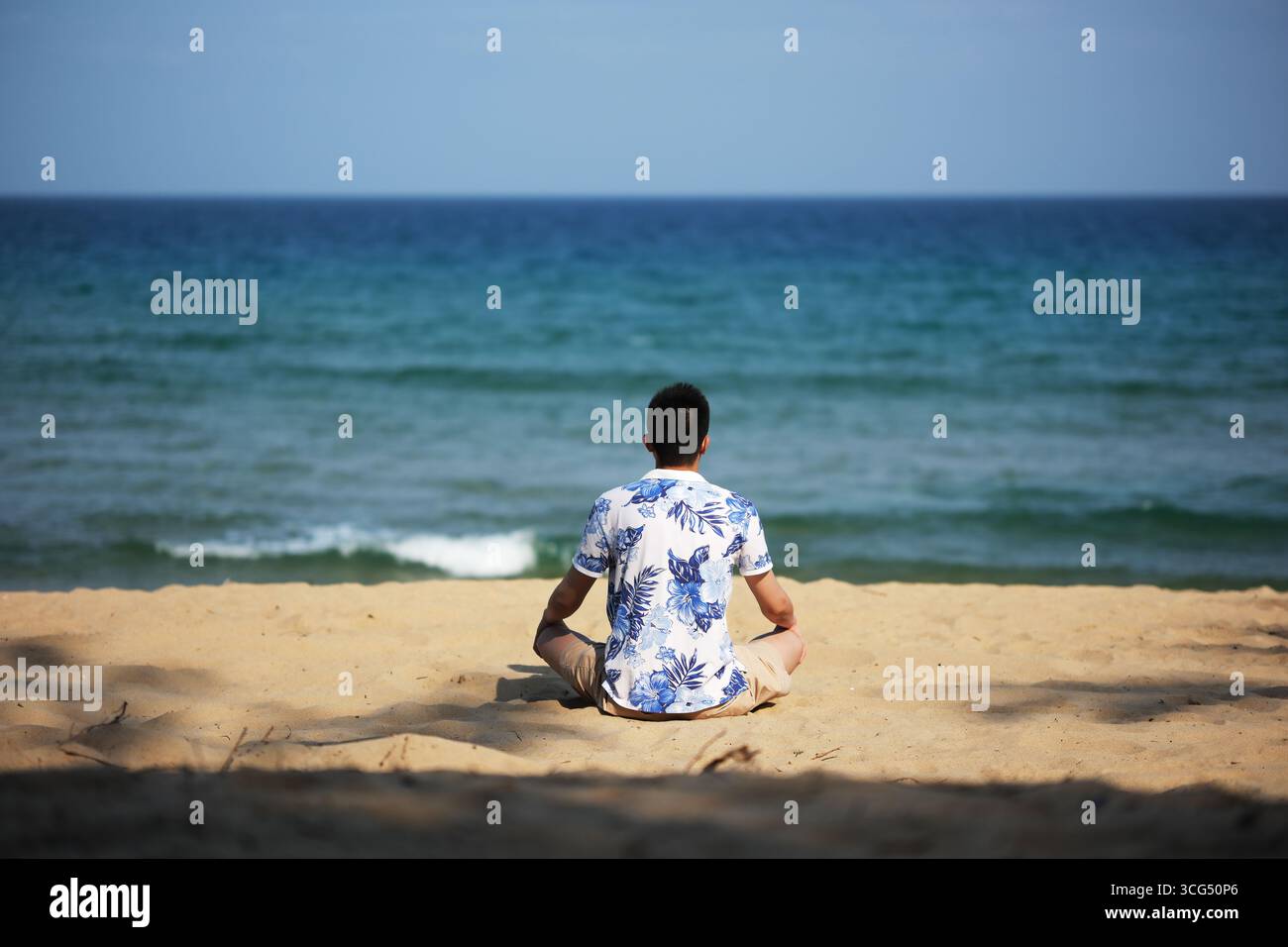 Mann, der am Strand sitzt und auf den Ozean blickt. In Sanya, Hainan, China Stockfoto