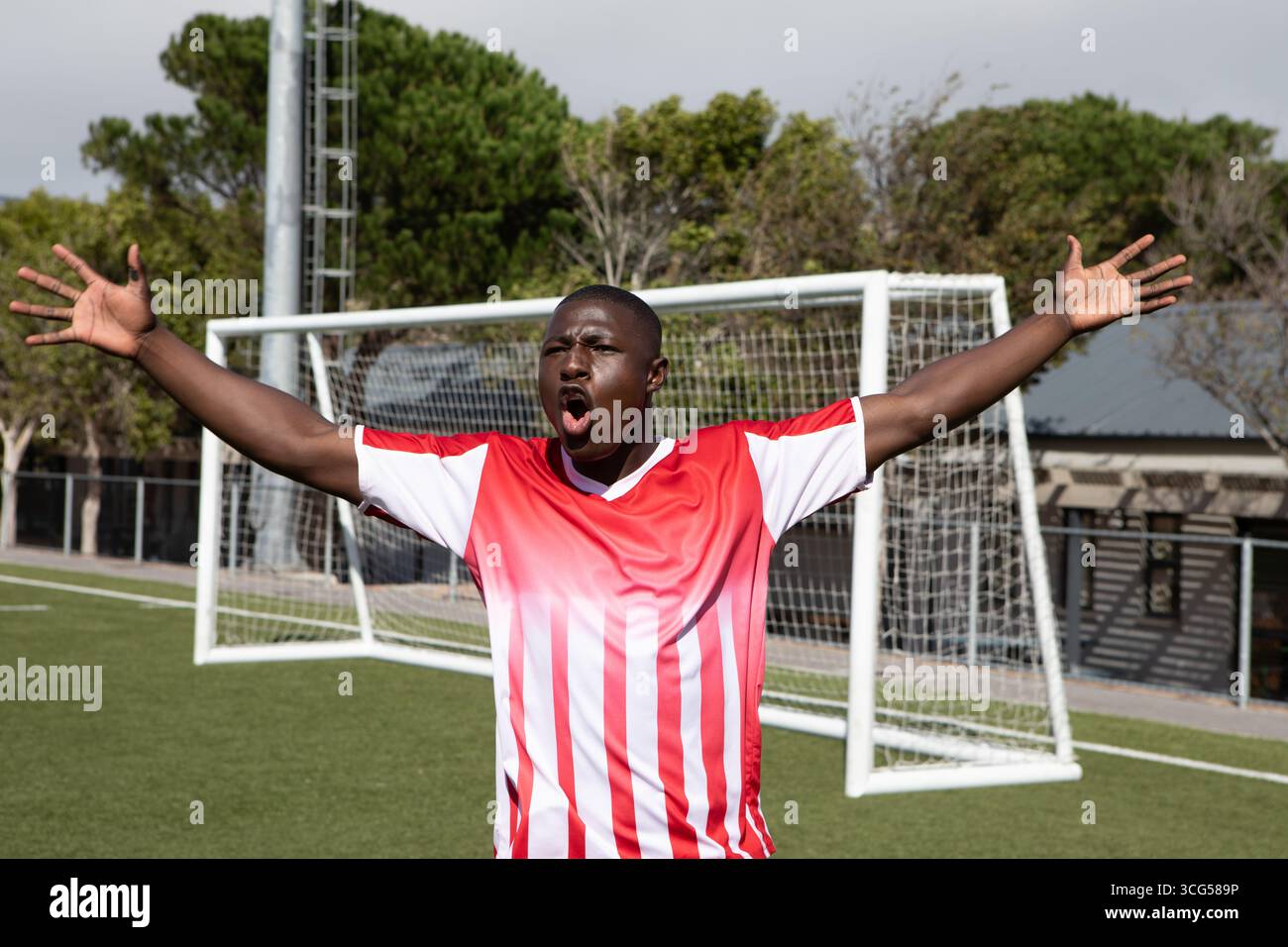 Afroamerikanischer Mann, der auf Kunstrasen mit Fußballtor in rotem Jersey feiert Stockfoto