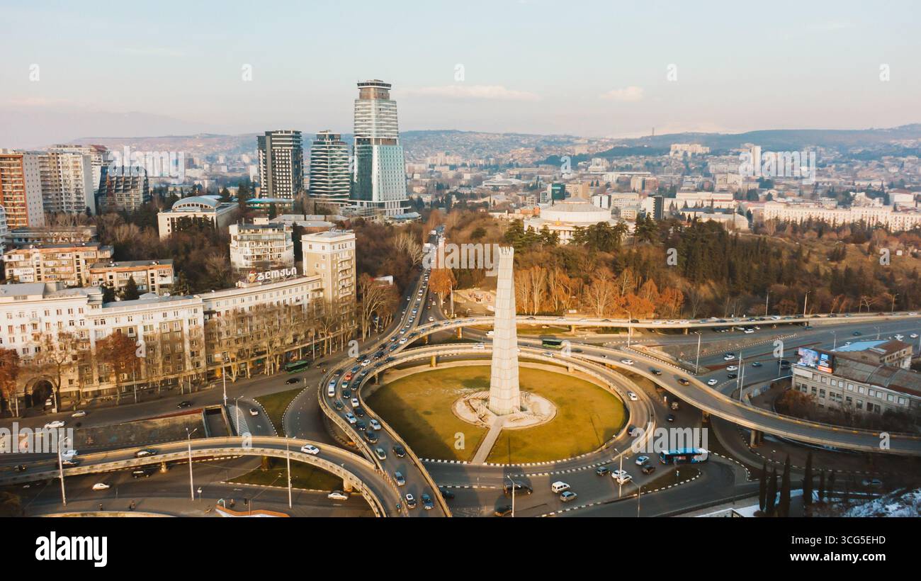 Blick aus der Vogelperspektive auf den Heldenplatz in tiflis, georgia, mit Blick auf den belebten Verkehr, der an einem sonnigen Tag durch den Kreisverkehr und die umliegende Stadtlandschaft navigiert Stockfoto