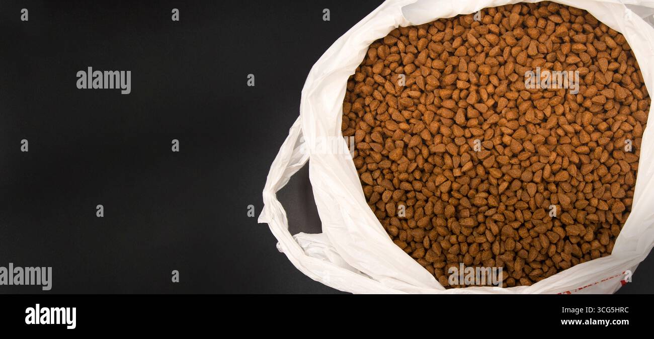 Nahaufnahme von Trockenfutter für Haustiere in weißem Plastikbeutel isoliert auf schwarzem Hintergrund Konzept von Katzenfutter Hundefutter Tierernährung und Tierpflege Stockfoto