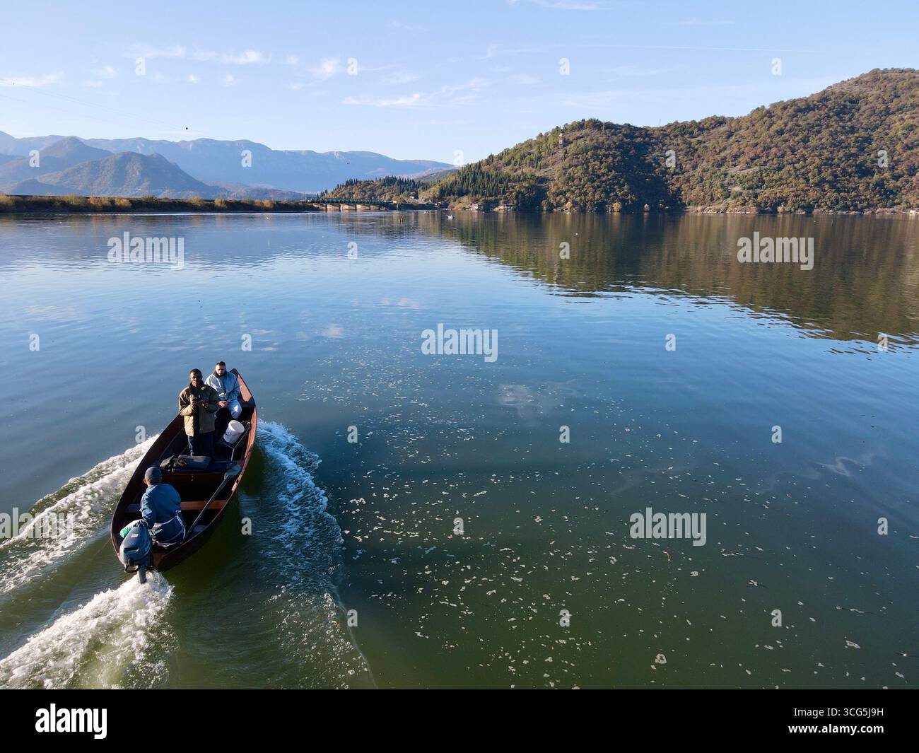 Skadar Lake (TGD), Montenegro – 2020.11.08: Afrikanischer Alleinreisender in einem Holzboot mit lokalen Gastgebern während des Airbnb Fishing Experience in der Nähe von Virpazar. Stockfoto