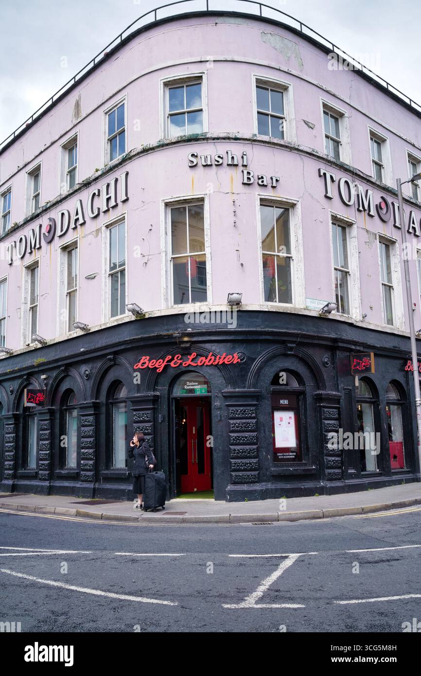 Ein pinkfarbenes Gebäude mit der Aufschrift „TOMODACHI Sushi Bar“ in Irland, ein Restaurant mit einem „Beef & Lobster“-Restaurant unten. Stockfoto