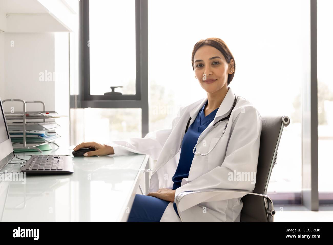 Positiv zuversichtliche junge Ärztin am Arbeitsplatz Stockfoto