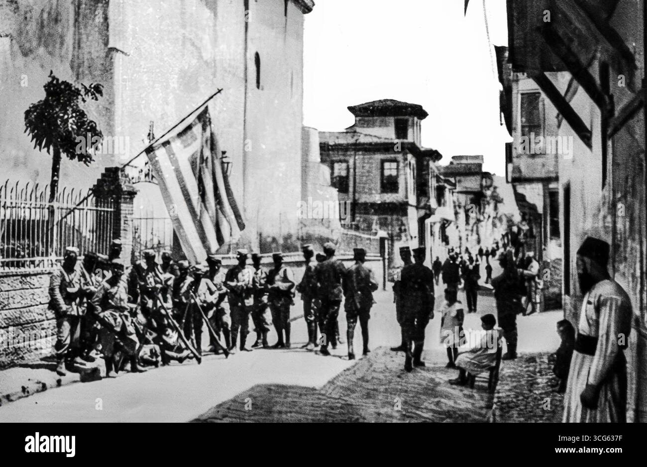 Ein französischer Militärposten in einer Straße von Salonica, Juni 1916. Soldaten patrouillieren und stehen Wache, mit Flaggen, die die Präsenz der Alliierten in der belagerten Stadt markieren. Dieses Bild zeigt die alltägliche Realität der Besatzung während des Ersten Weltkriegs, wo städtische Räume militarisiert wurden. Als Teil der mazedonischen Front wurde Salonica zu einem zentralen Drehkreuz für Entente-Operationen und unterstrich die strategische Rolle Griechenlands im weiteren Konflikt. Stockfoto Ein französischer Militärposten in einer Straße von Salonica, Juni 1916. Soldaten patrouillieren und stehen Wache, mit Flaggen, die die Präsenz der Alliierten in der belagerten Stadt markieren. Dieses Bild zeigt die alltägliche Realität der Besatzung während des Ersten Weltkriegs, wo städtische Räume militarisiert wurden. Als Teil der mazedonischen Front wurde Salonica zu einem zentralen Drehkreuz für Entente-Operationen und unterstrich die strategische Rolle Griechenlands im weiteren Konflikt. Stockfoto
