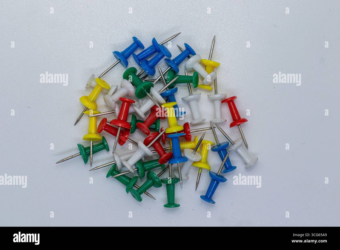 Sammlung von bunten Stecknadeln in Grün, Rot, Blau, Gelb und weiß, auf einer neutralen Oberfläche verstreut. Wichtige Schreibwaren zum Anheften von Notizen, Stockfoto