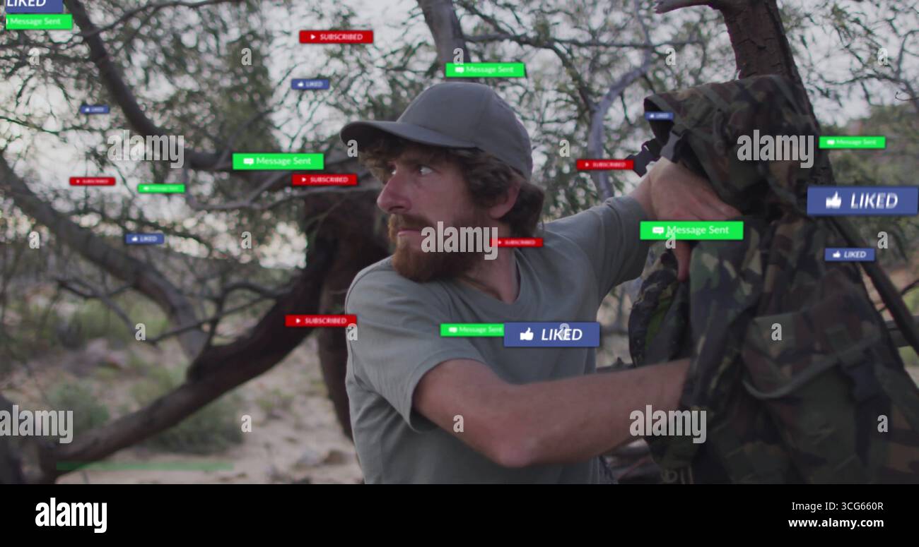 Stehender bärtiger Mann mit Tarnjacke in trockenem Gestrüpp, mit schwebenden Social-Media-Ikonen Stockfoto