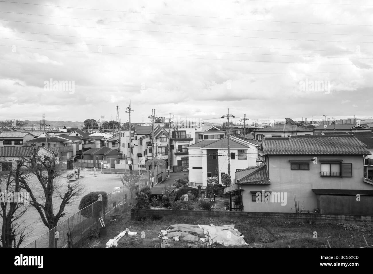 Einfarbige Aufnahme einer ruhigen Wohngegend in Japan mit traditionellen Häusern unter einem bedeckten Himmel und Bäumen im Vordergrund, die ein ruhiges A schaffen Stockfoto