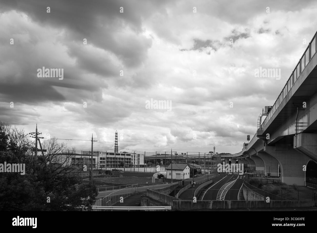 Schwarzweiß-Foto mit einer urbanen Szene mit einer erhöhten Autobahn, Industriebauten und einem dramatischen bewölkten Himmel in Osaka, Japan Stockfoto