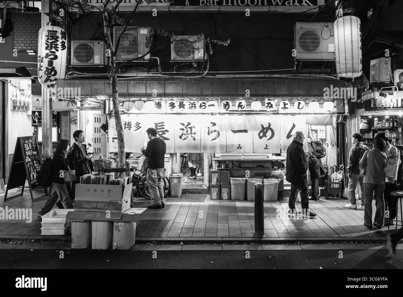 In einer belebten Street-Food-Szene in Kyoto treffen sich Menschen vor einem traditionellen Ramen-Shop unter leuchtenden Lichtern und erwecken so ein Gemeinschaftsgefühl Stockfoto